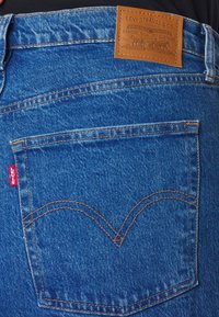 Blue denim jeans back pocket with orange stitching, red Levi's tag, and tan leather Levi Strauss & Co. brand patch above pocket.