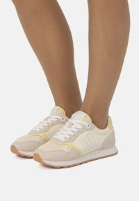 Scarpe da ginnastica beige e gialle con tomaia in mesh e camoscio, punta tonda, collo imbottito, lacci bianchi e suola in gomma.