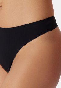 Bas de bikini noir avec une texture lisse, une coupe haute et une ceinture minimaliste, affichant une couleur unie sans motifs.