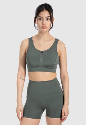 Green athletic bra with front zipper, wide straps, and seamless design, paired with matching high-waisted shorts featuring a smooth texture.