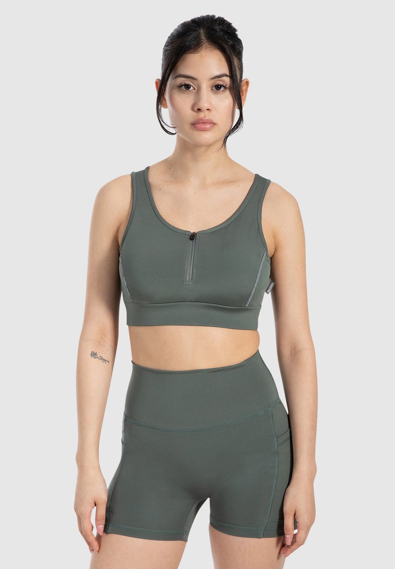 Zelený sportovní podprsenka s předním zipem, širokými ramínky a bezešvým designem, doplněná o odpovídající vysoké šortky s hladkou texturou.