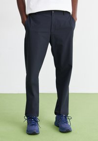 Mørkeblå bukser med en glat overflade, lige pasform og sidelommer, suppleret med en hvid skjorte og blå sneakers.