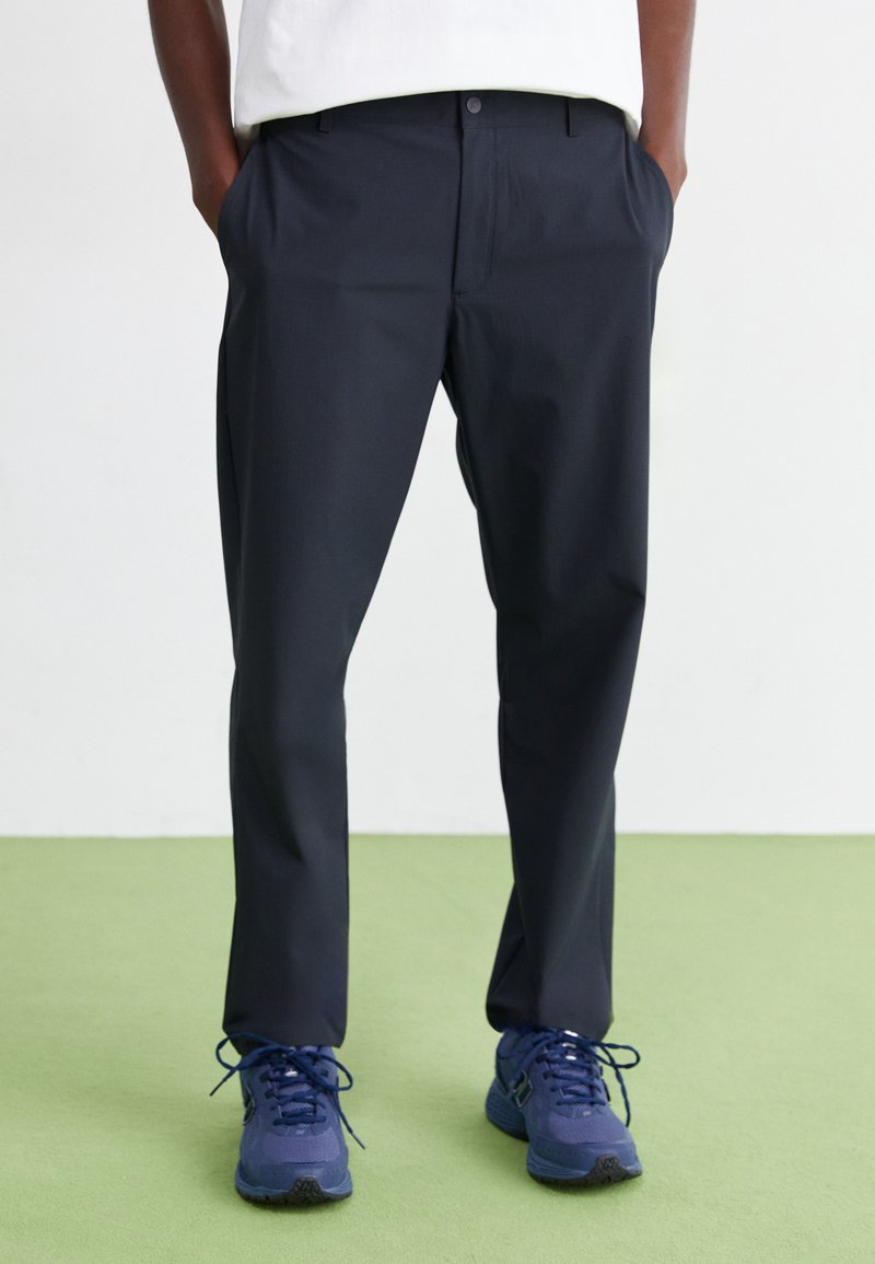 Mørkeblå bukser med en glat overflade, lige pasform og sidelommer, suppleret med en hvid skjorte og blå sneakers.