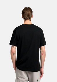Camiseta de algodón negra con un clásico cuello redondo y mangas cortas. La parte trasera es sencilla, sin gráficos ni patrones visibles.