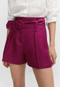 Fuchsia maßgeschneiderte Shorts mit einem breiten Gürtel und einer runden Schnalle, plissierter Gestaltung und strukturiertem Stoff, kombiniert mit einem weißen Hemd.