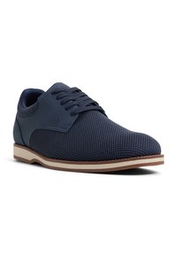 Zapatos de malla azul oscuro con acentos sintéticos suaves, puntera redonda y suela de goma marrón con una sutil línea clara.