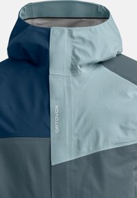 Water-resistant jacket in light blue and navy colors. Features a high collar, angular design, and logo detail in white on the side.