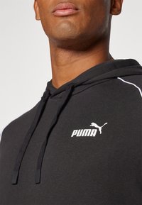 Black hooded sweatshirt with white Puma logo, textured fabric, and contrasting white piping along the seams. Drawstring closure at the hood.