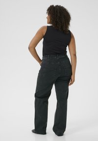 Black sleeveless top paired with high-waisted, straight-leg dark jeans. Visible back pockets and seams, featuring a soft, textured denim fabric.