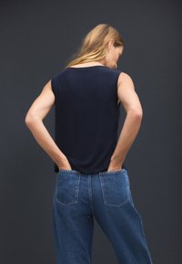 Marineblaues, ärmelloses Oberteil aus leichtem Material, kombiniert mit hoch taillierter blauer Jeans mit aufgesetzten Gesäßtaschen und lockerem Schnitt.