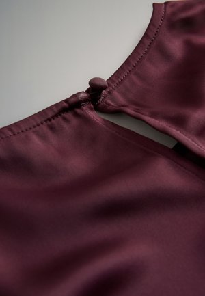 Burgundia satiinist top, millel on tagaküljel võtmeauguga sulgur, ümara kangaga kaetud nupu ja siledalt läikiva tekstuuriga.