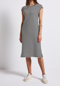 Svartvit randig midiklänning med korta ärmar, ribbad struktur, sidenslitsdetaljer och kombinerad med vita sneakers för en avslappnad look.