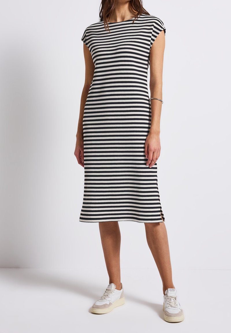 Svartvit randig midiklänning med korta ärmar, ribbad struktur, sidenslitsdetaljer och kombinerad med vita sneakers för en avslappnad look.