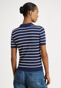 Modro-biele pruhované polo tričko s krátkym rukávom, so žebrovaným golierom a lemom. Mäkká textúra, priliehavý strih a minimálne kovové prvky.