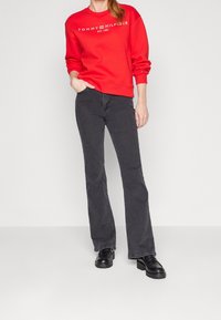 Czerwona bluza z białym logo, zestawiona z ciemnoszarymi rozszerzanymi dżinsami. Czarne masywne buty. Gładka faktura, casualowy krój.