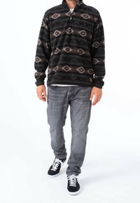Svart och grå fleecetröja med halvvagn, med diamantmönster och en strukturerad yta, i kombination med grå jeans och svarta sneakers.