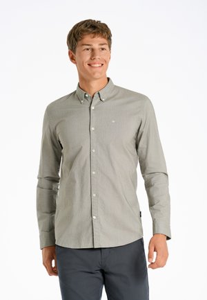 Camisa de botones verde claro con una textura sutil y mangas largas, que presenta un pequeño logo en el pecho, combinada con pantalones oscuros.