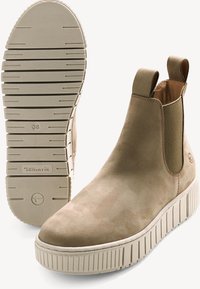 Bottes chelsea en suède de couleur tan avec une insert élastique texturé, des tirants et une semelle en caoutchouc ridée de couleur blanc cassé. Taille 38 indiquée sur la semelle.