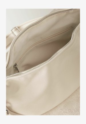 Bežinės odinės kuprinės vidus, su užtrauktuku kišene ir lygaus audinio pamušalu. Kuprinė turi apvalią formą ir sidabrinius aksesuarus.