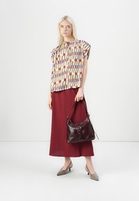 Patterned short-sleeve top in beige, maroon, and green; floor-length maroon skirt; burgundy leather handbag; grey heeled shoes.