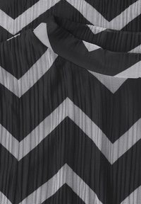Černobílá pruhovaná látka se vzorem cik-cak, má texturovaný, plisovaný design. Materiál působí lehce a prodyšně.