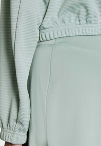 Jasnozielony strój sportowy z teksturowaną tkaniną na górze i gładkim wykończeniem na dole, z elastycznymi ściągaczami i detalami przeszyć.