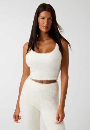 Top crop bianco soffice realizzato in tessuto morbido, con scollatura rotonda e spalline spesse, abbinato a pantaloni a vita alta coordinati.