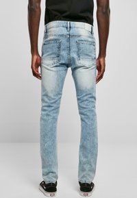 Jeans de mezclilla azul claro con un lavado descolorido, con bolsillos de parche y un diseño de pierna recta. Llevados con zapatillas negras.