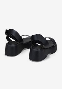 Sandalias de plataforma negras con dos correas anchas cruzadas, hechas de un material suave, que cuentan con una suela texturizada y un tacón grueso y curvado.