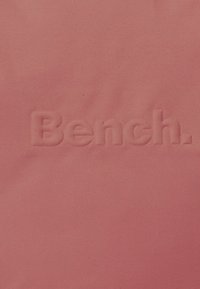 Koraal kleurige stof met een reliëf "Bench." logo. De textuur is glad, met een matte afwerking en een uniforme kleur.