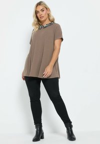 Tunique marrone a coste con maniche corte e colletto in stampa leopardata, abbinata a pantaloni neri attillati e stivaletti neri chunky.