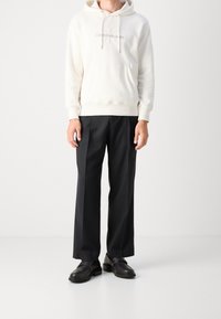 Krämfärgad hoodie med snörning och framficka, kombinerad med svarta vida byxor och svarta loafers. Enkelt mönster och rena linjer.