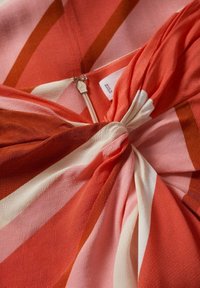 Gros plan d'un tissu rayé rouge, rose et blanc torsadé au centre avec une fermeture éclair argentée visible et une étiquette de vêtement.