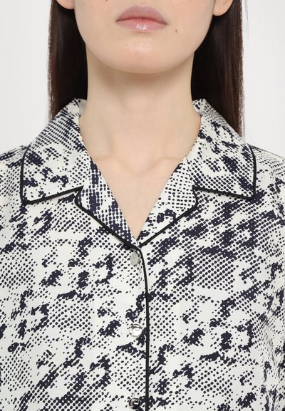 Camicia bianca con stampa astratta nera, caratterizzata da un colletto, maniche corte e chiusura con bottoni. Tessuto simile alla satin, con un bordo a contrasto.