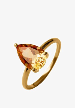 Anillo de oro con una gema naranja en forma de pera sostenida por tres garras sobre una banda lisa y pulida contra un fondo blanco.