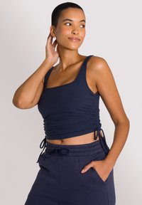 Top corto a righe navy con lacci laterali regolabili e scollatura quadrata, abbinato a jogger navy con logo ricamato e vita elastica.