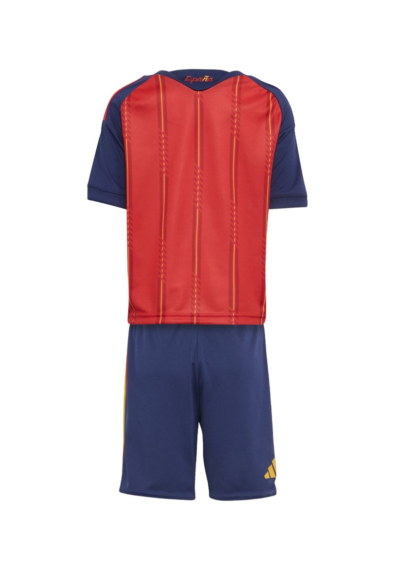 Σετ ποδοσφαίρου σε κόκκινο και ναυτικό μπλε, που περιλαμβάνει κοντομάνικο μπλουζάκι με κάθετες λεπτομέρειες και κίτρινες αποχρώσεις, συνδυασμένο με αντίστοιχο σορτς.