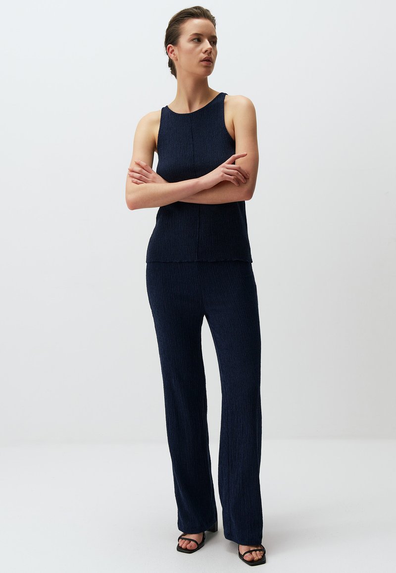 Completo due pezzi navy realizzato in tessuto texturizzato, composto da un top senza maniche e pantaloni a gamba larga. Accentuato da un orlo sfrangiato.