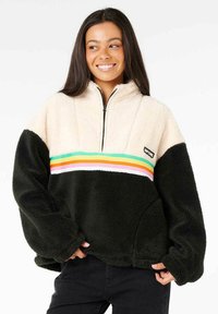 Flauschiger Pullover mit creamfarbener Oberseite und schwarzem Unterteil, der ein mehrfarbig gestreiftes Band über die Brust und einen Reißverschlusskragen hat.