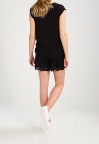 Schwarzes kurzärmeliges Oberteil kombiniert mit schwarzen Shorts mit Spitze, getragen mit weißen Slippern, von hinten betrachtet.