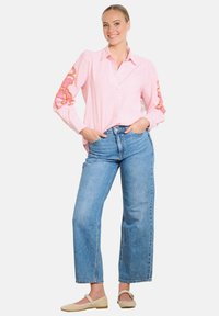 Dryžuota rožinė mygtukų marškinė su gėlėmis siuvinėjimu ant rankovių, derinama su aukštu liemeniu mėlynomis džinsomis ir šviesios spalvos plokščiadugniais batais.