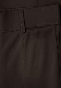 Gros plan sur un tissu brun foncé avec une passants de ceinture et des détails de couture horizontale et verticale, probablement une partie d'une ceinture de vêtement.