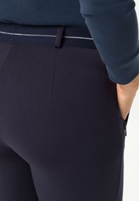 Marineblauwe broek met een gladde textuur, voorzien van een contrasterende witte accent op de tailleband en een zijzak met rits.