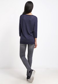 Mörkblå tröja med lös passform, ¾-långa ärmar och vita prickar. Matchad med grå skinny jeans och svarta sneakers.