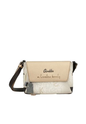 Beżowo-biała torba na ramię z klapką z napisem „Anekke a timeless beauty”, ozdobnym przeszyciem oraz ciemnym, regulowanym paskiem na ramię.