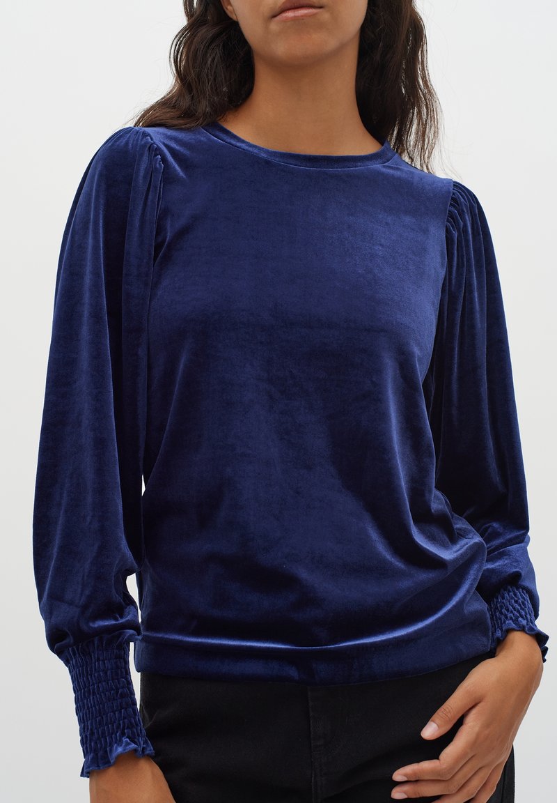 Námořnická sametová blůza s dlouhými rukávy, nafouknutými rameny a smockovanými manžetami. Měkká textura s uvolněným střihem a kulatým výstřihem.