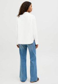 Witte long sleeve shirt met een yoke-design, gecombineerd met lichtblauwe flared jeans, met een vervaagde textuur en een rechte achterkant.