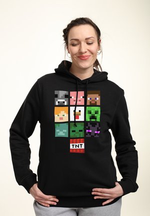 Czarna bluza z kapturem z graficznym wzorem pikselowych postaci, w tym zwierząt i figur, z czerwoną i białą metką "TNT" na dole.