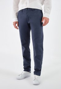 Marineblauwe chino's van een katoenmix, met een recht model, voorzakken en een enkele knoopsluiting aan de voorkant, gecombineerd met witte sneakers.