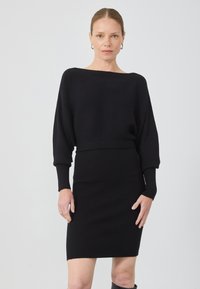 Rochie tricotată neagră, cu un decolteu larg, mâneci lungi și textură cu nervuri. Siluetă ajustată cu o lungime până la genunchi.